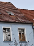 Foto: Große Holzlatte liegt auf den Dachziegeln eine verkommenen Hauses  