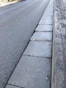 Foto: mehrere defekte Platten zwischen Straßenbelag und Bürgersteigkanten 